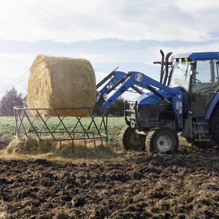 Boy farmer removing netting from hay stack in dairy farm field